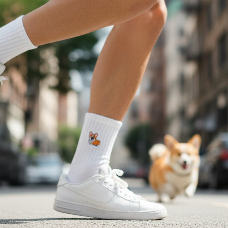 Person wearing white sneakers with a dog in the background on a city street.