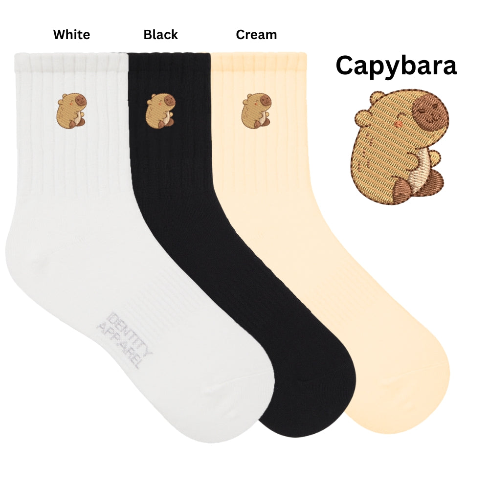Three pairs of socks in white, black, and cream with a capybara design on a white background.