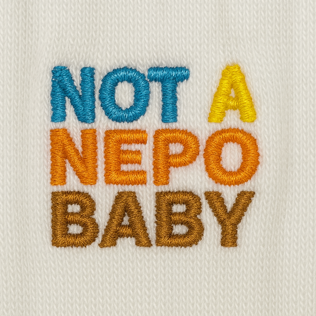 Embroidered text 'NOT A NEPO BABY' on a beige background