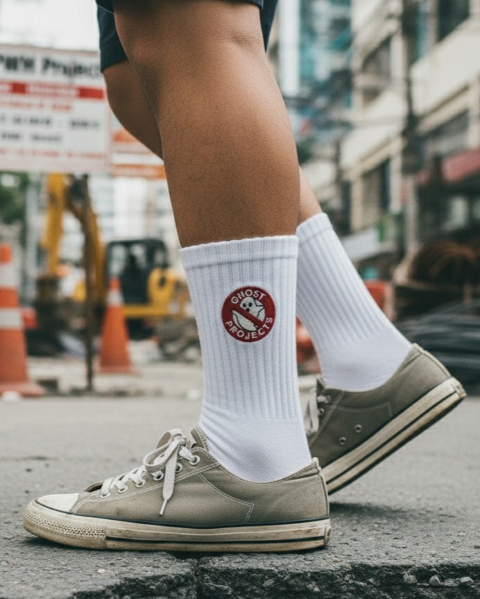 Person wearing white socks with a logo and brown sneakers on an urban street.