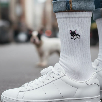 White sneakers and rolled-up jeans with a sock featuring a small logo on a blurred street background
