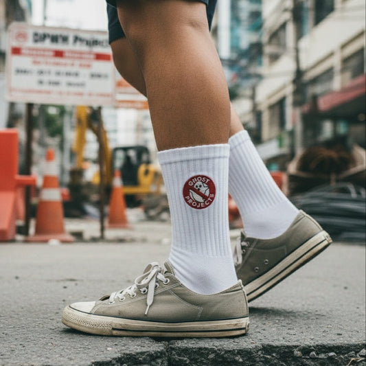 Person wearing white socks with a logo and brown sneakers on an urban street.