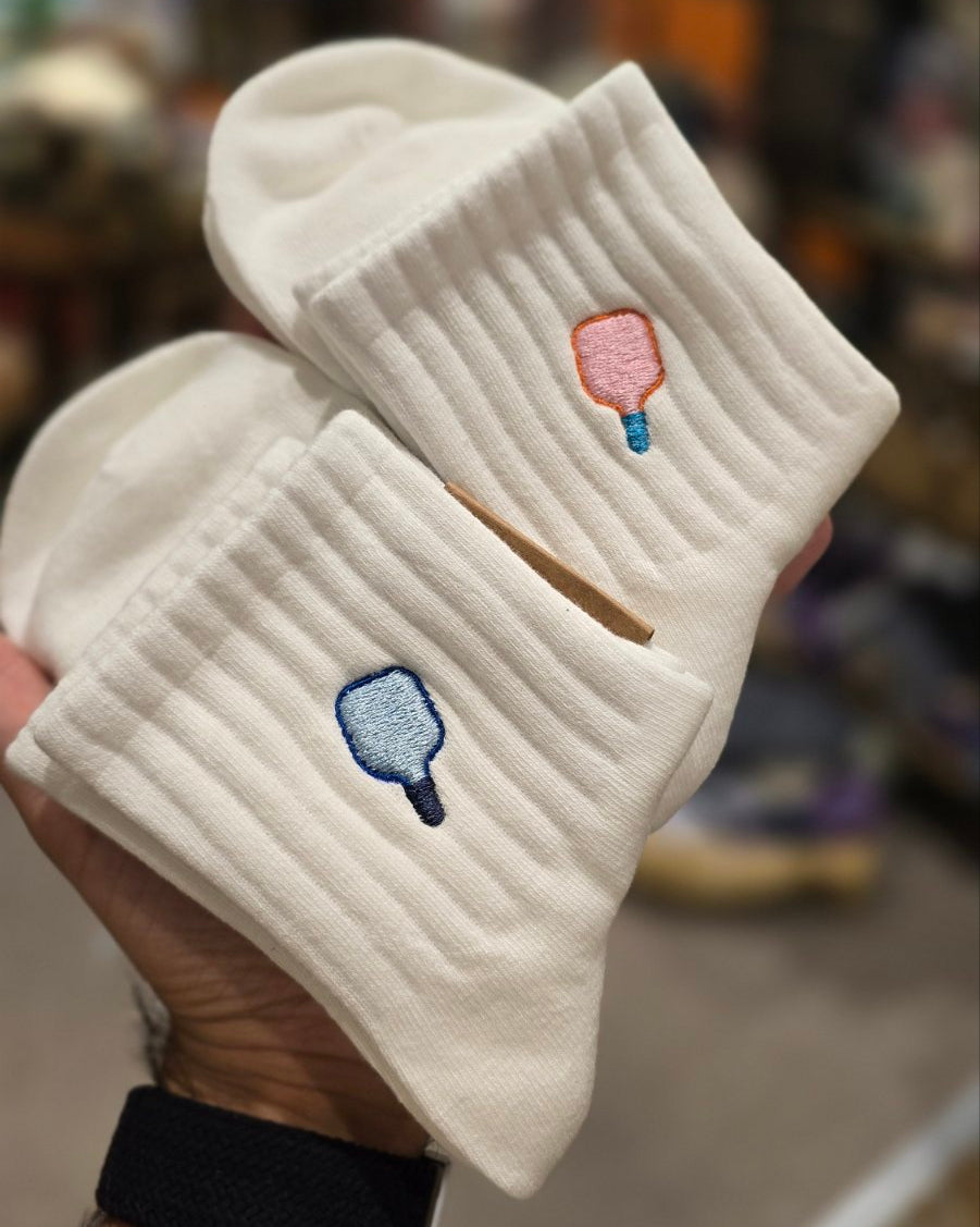 White socks with paddle ball designs held by a hand in a store setting