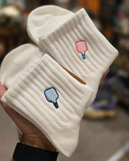 White socks with paddle ball designs held by a hand in a store setting