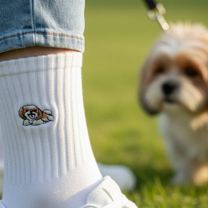 White sock with a dog design worn by a person on grass, with a dog in the background.