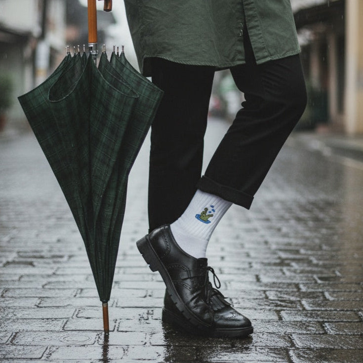 Person holding a green umbrella on a rainy street, wearing a green coat and black shoes.